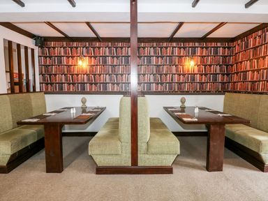 A dining area with green upholstered booth seating and wooden tables with wallpaper showing bookshelves at The Five Bells Inn in Upwell
