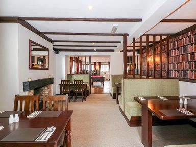 A dining area with wooden tables and chairs a fireplace and a pool table in the background at The Five Bells Inn in Upwell