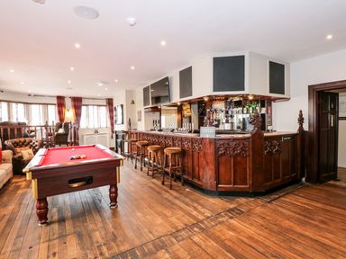 A bar area with stools a red pool table and seating near windows at The Five Bells Inn in Upwell