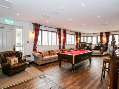 A seating area with sofas and armchairs around a pool table in a room with wooden floors and plaid curtains at The Five Bells Inn in Upwell