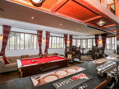 A game room with a red pool table brown leather chairs and a bar area at The Five Bells Inn in Upwell