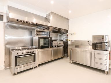 A commercial kitchen with stainless steel appliances including ovens, stovetop, and microwaves at The Five Bells Inn in Upwell