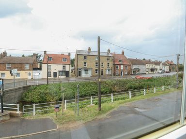 A street with houses along a road and a small river bordered by railings at The Five Bells Inn in Upwell