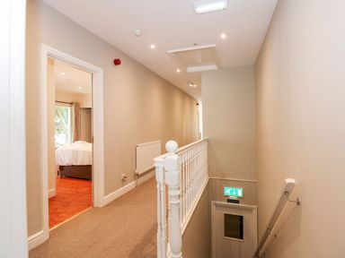 A hallway with carpeted floor a staircase with white railing and a room with bed visible at The Five Bells Inn in Upwell