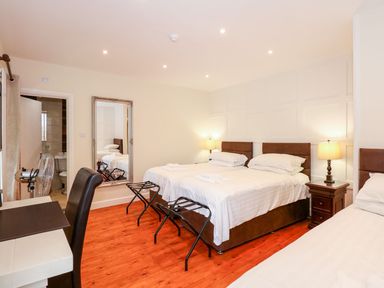 A bedroom with two double beds and one single bed a desk chair a large mirror and bedside tables at The Five Bells Inn in Upwell
