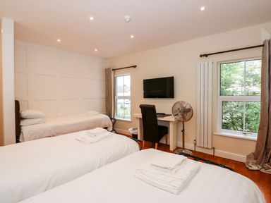 A bedroom with three single beds a desk with a chair a wall-mounted television and two windows at The Five Bells Inn in Upwell