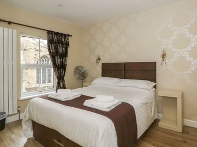 A bedroom with a double bed two folded towels bedside tables a window and a standing fan at The Five Bells Inn in Upwell