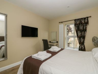 A bedroom with a bed and towels on it a wall mounted TV a desk with a chair and a window with curtains at The Five Bells Inn in Upwell