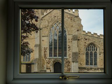 A view of a stone church with arched windows seen through a window frame at The Five Bells Inn in Upwell