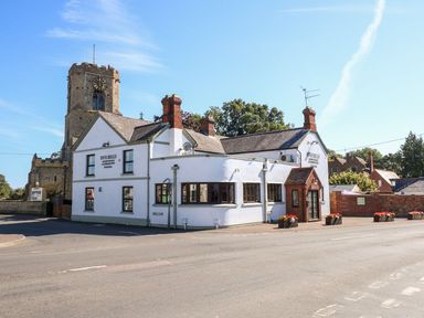 A white building with chimneys and flower pots outside next to a stone clock tower at The Five Bells Inn in Upwell