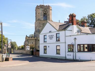 A street view with a white building named Five Bells and a church tower behind it at The Five Bells Inn in Upwell