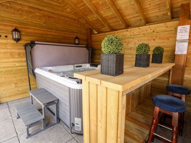 A wooden outdoor area with a hot tub small steps a wooden bar with potted plants and bar stools at The Five Bells Inn in Upwell