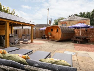 An outdoor patio area with lounge chairs a covered seating area a wooden barrel-shaped structure and a picnic table with umbrella at The Five Bells Inn in Upwell