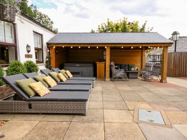 An outdoor patio area with lounge chairs and cushions next to a covered seating area with chairs and a table at The Five Bells Inn in Upwell