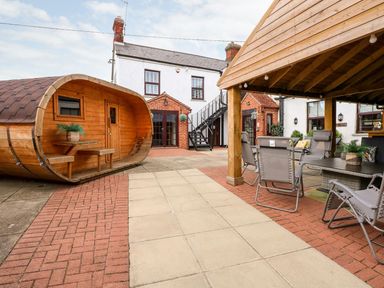 An outdoor patio area with a wooden barrel-shaped seating pod and covered seating with chairs at The Five Bells Inn in Upwell