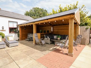 An outdoor seating area with a wooden roof structure and lounge chairs at The Five Bells Inn in Upwell