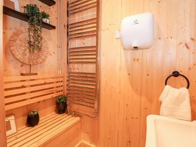 A small wooden room with a bench a sink a towel ring with a white towel a hand dryer and plants on shelves at The Five Bells Inn in Upwell