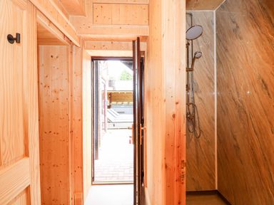 A wooden hallway with a door leading outside and a shower area with marble walls