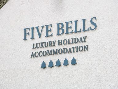 A white wall with a sign reading Five Bells Luxury Holiday Accommodation and five bell icons below at The Five Bells Inn in Upwell