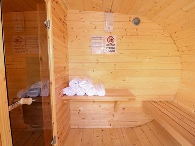 A wooden sauna interior with a bench a wooden shelf holding rolled white towels and a glass door at The Five Bells Inn in Upwell