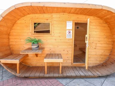 A wooden sauna cabin with an open door a small table and two benches outside and a plant on the table at The Five Bells Inn in Upwell