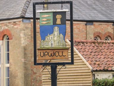 A wooden village sign with a church and fish hanging outside buildings at The Five Bells Inn in Upwell