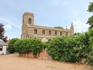 A stone church with a tower behind a brick wall covered with green ivy at The Five Bells Inn in Upwell