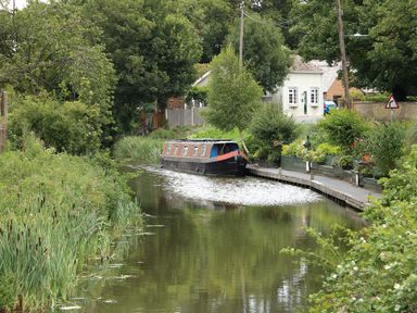 A narrowboat moored along a canal with greenery and houses in the background at The Five Bells Inn in Upwell