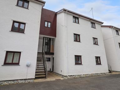 Exterior view of a white multi-story apartment building with brown framed windows and an outdoor staircase at 9 Oakley Wharf in Porthmadog