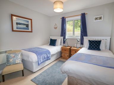 A bedroom with two single beds side by side with blue cushions and blankets and wooden bedside tables in between at 9 Oakley Wharf in Porthmadog