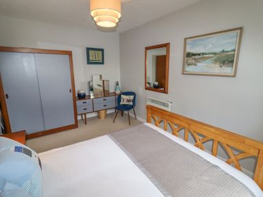 A bedroom with a wooden bed, blue chair, dresser with mirror, and paintings on the walls at 9 Oakley Wharf in Porthmadog