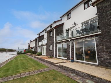 A row of terraced houses with balconies and sliding glass doors facing a riverside lawn at 9 Oakley Wharf in Porthmadog