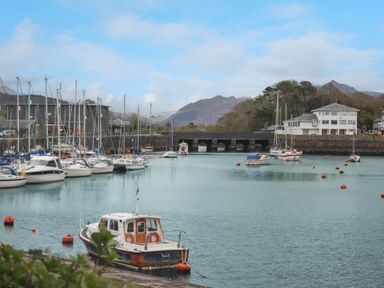 A harbor with multiple boats docked and a stone bridge in the background at 9 Oakley Wharf in Porthmadog