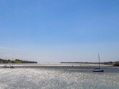 A body of water with sailboats and a coastline with trees at 9 Oakley Wharf in Porthmadog