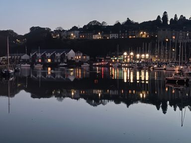 A marina with boats docked and buildings with lights reflecting on calm water at 9 Oakley Wharf in Porthmadog