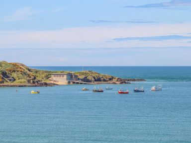 A coastal scene with several boats floating on the water near a rocky shore with a building on the land at Sea Cliff in Morfa Nefyn