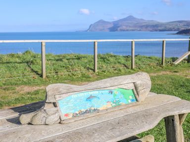 A wooden bench with an informational sign and a view of the sea and mountains at Sea Cliff in Morfa Nefyn