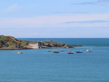A coastal scene with several boats on the water and a building on a grassy hill at Sea Cliff in Morfa Nefyn