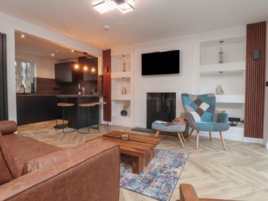 A living room with a brown leather sofa a wooden coffee table a patterned armchair a fireplace and a mounted TV at Sea Cliff in Morfa Nefyn
