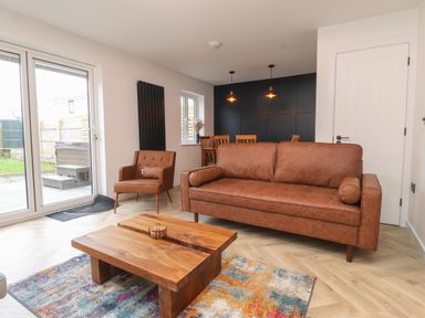 A living room with a brown sofa a brown armchair a wooden coffee table colorful rug and dining area at Sea Cliff in Morfa Nefyn