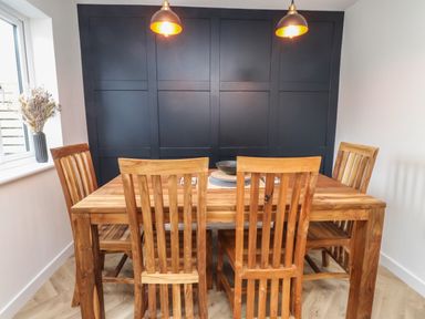 A dining room with a wooden table four wooden chairs two pendant lights and a black paneled wall at Sea Cliff in Morfa Nefyn