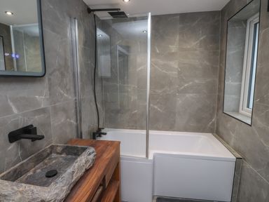 A bathroom with a stone sink on a wooden counter and a bathtub with glass shower screen at Sea Cliff in Morfa Nefyn