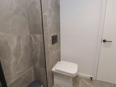 A bathroom with a white toilet a black flush panel and grey marble tiled walls at Sea Cliff in Morfa Nefyn