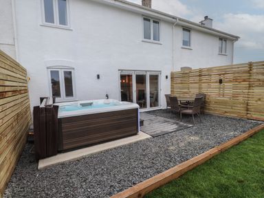 An outdoor area with a hot tub table and chairs fenced yard at Sea Cliff in Morfa Nefyn