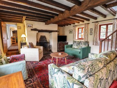A living room with wooden ceiling beams sofas and a fireplace at The Long House in Penmachno