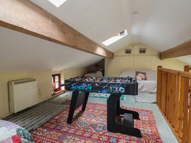 A loft room with a foosball table sofas with cushions and wooden ceiling beams at The Long House in Penmachno