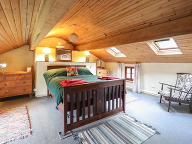A bedroom with a wooden bed green bedding and red towels under skylight windows at The Long House in Penmachno