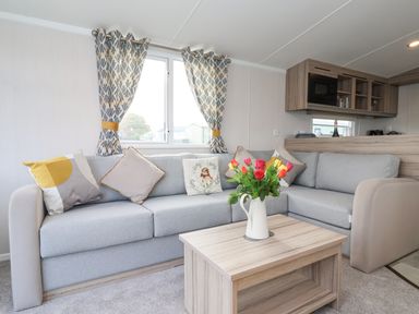 A living room with a grey sectional sofa cushions and a wooden coffee table with flowers at Lazy Dayz Lodge in East Heslerton near Malton
