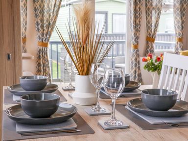 A dining table set with dark gray bowls and plates wine glasses and a white vase with dried plants at Lazy Dayz Lodge East Heslerton near Malton