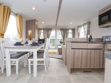 A dining area with a table set with glasses and plates next to a kitchen with wooden cabinets at Lazy Dayz Lodge in East Heslerton near Malton